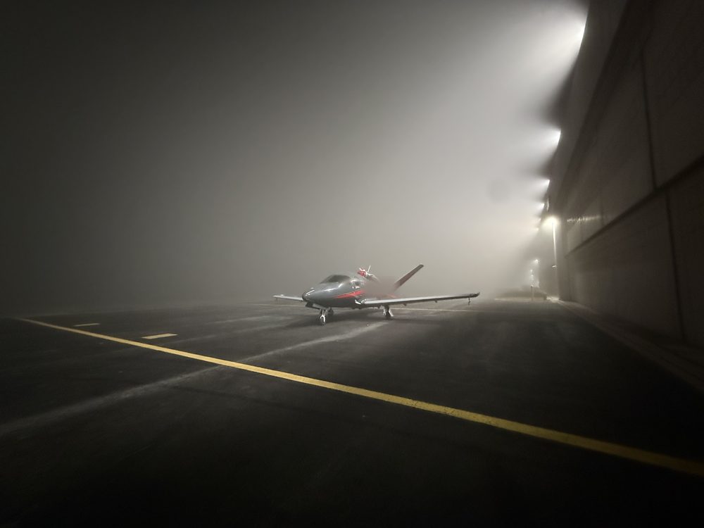 Cirrus SF50 Vision Jet on a foggy ramp at night beside a lit hangar